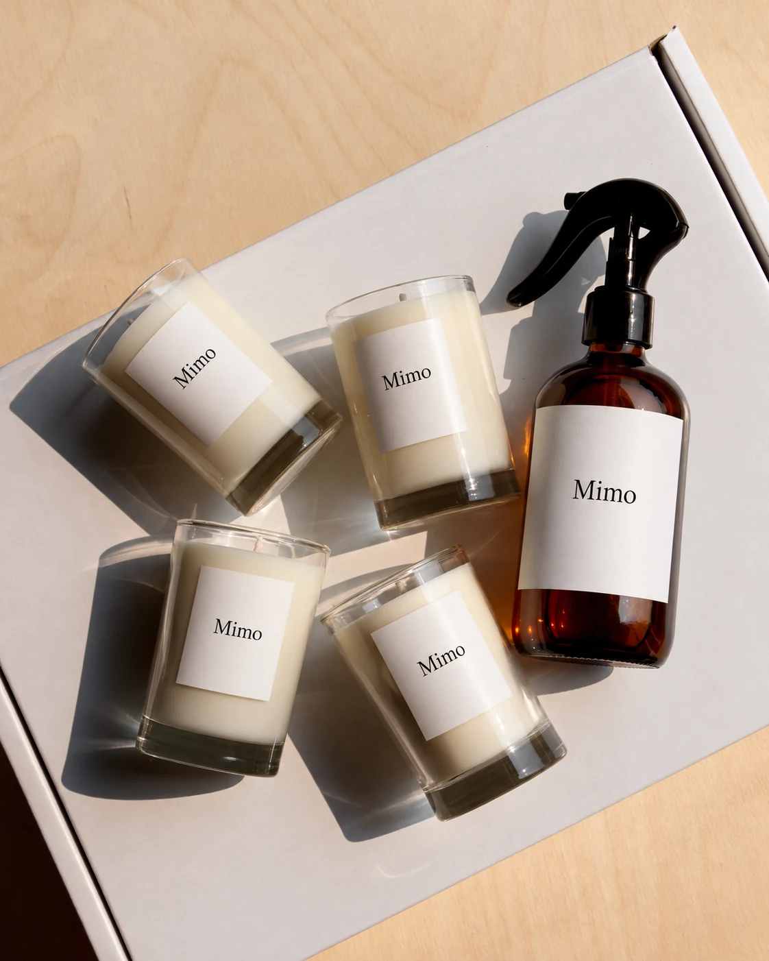 Four Mimo labelled glass candles and an amber spray bottle arranged on a white box